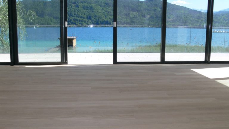 Blick auf einen See mit Bergen im Hintergrund, von einem modernen Raum aus sichtbar.