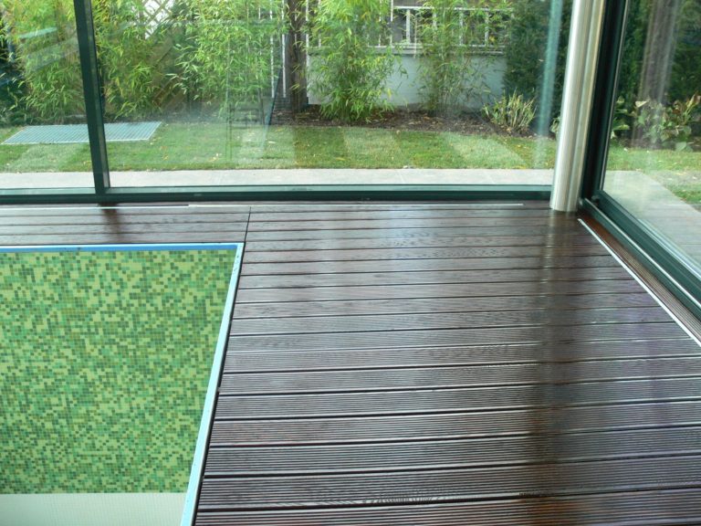 Holzboden in einem lichtdurchfluteten Raum mit einem grünen Teppichstück.