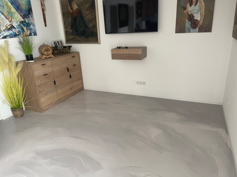 Wohnraum mit grauem Boden, TV an der Wand, Holzschrank und Pflanzen.