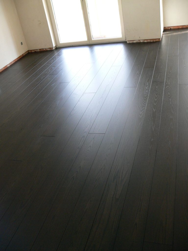 Dunkler Holzboden in einem leeren Raum mit Fenstern.