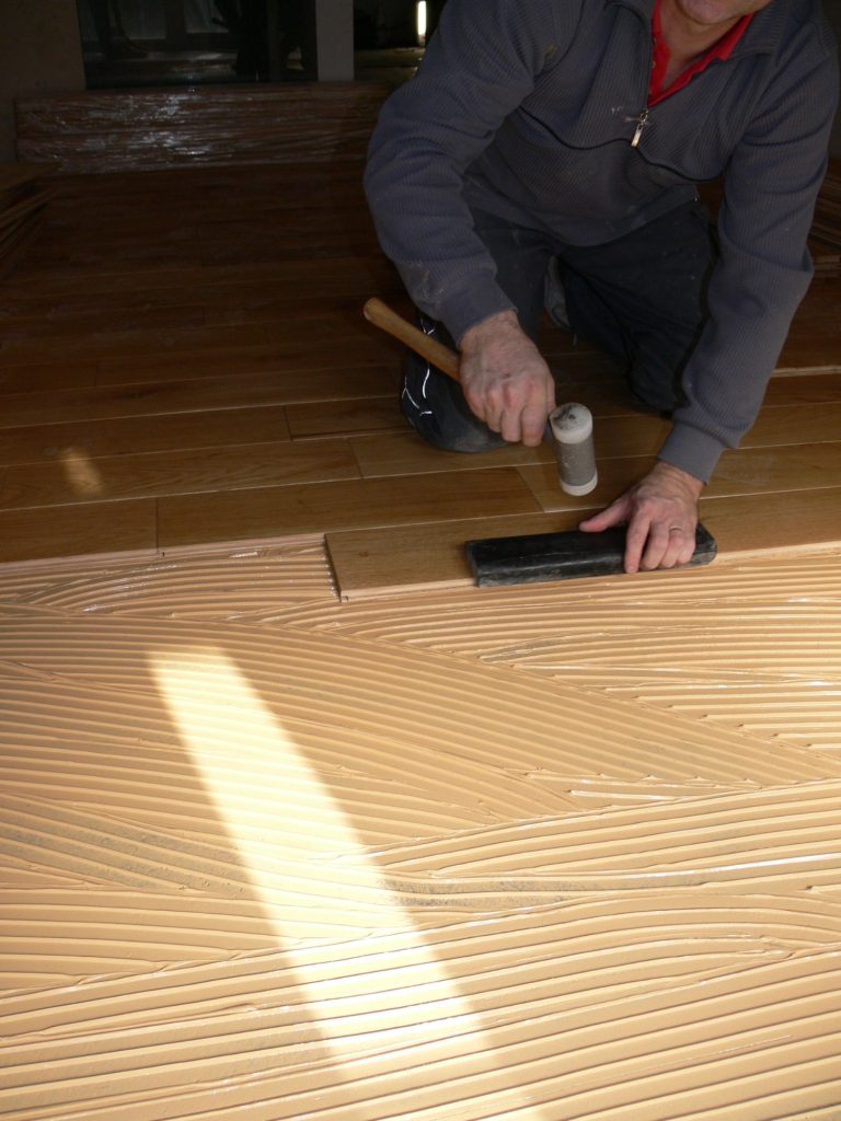 Eine Person verlegt Holzbohlen und klopft mit einem Hammer auf einen Rand.