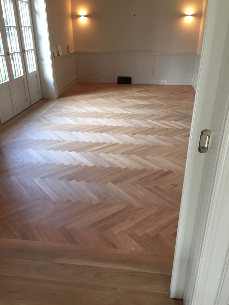 Holzboden verlegt im Fischgrätmuster, gut beleuchteter Raum mit Fenstern.