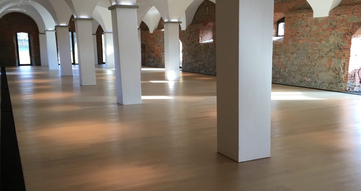 Heller, offener Raum mit Holzfußboden und säulengegliedertem Deckenbereich.