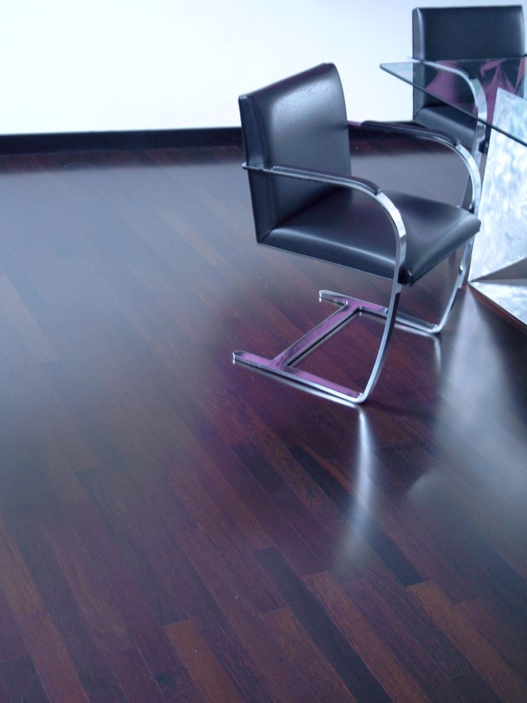 Schwarzer Stuhl aus Leder vor einer modernen Glastischoberfläche auf Parkettboden.